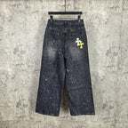 Dark denim pants with speckled finish and small white graphic cross on thigh