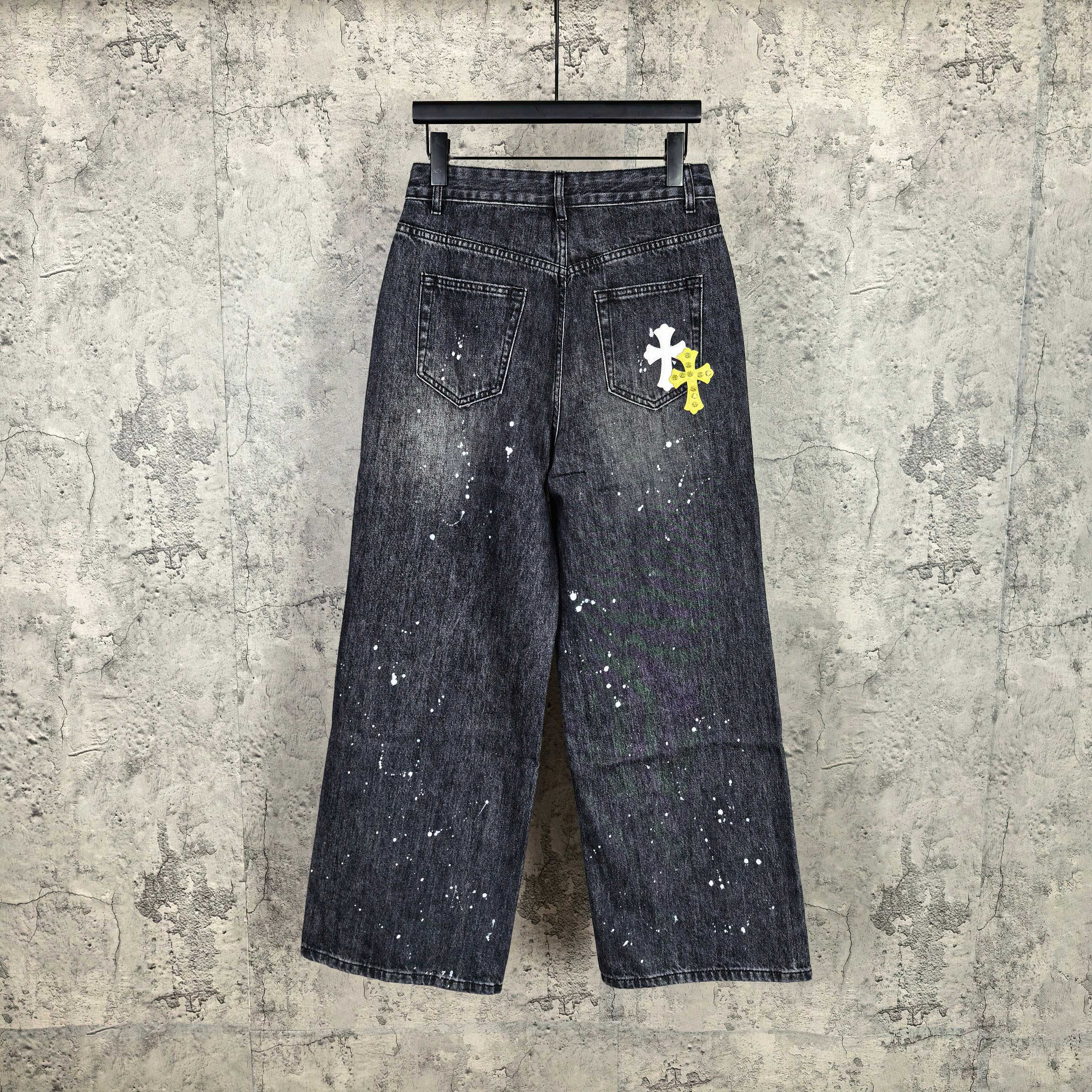 Dark denim pants with speckled finish and small white graphic cross on thigh