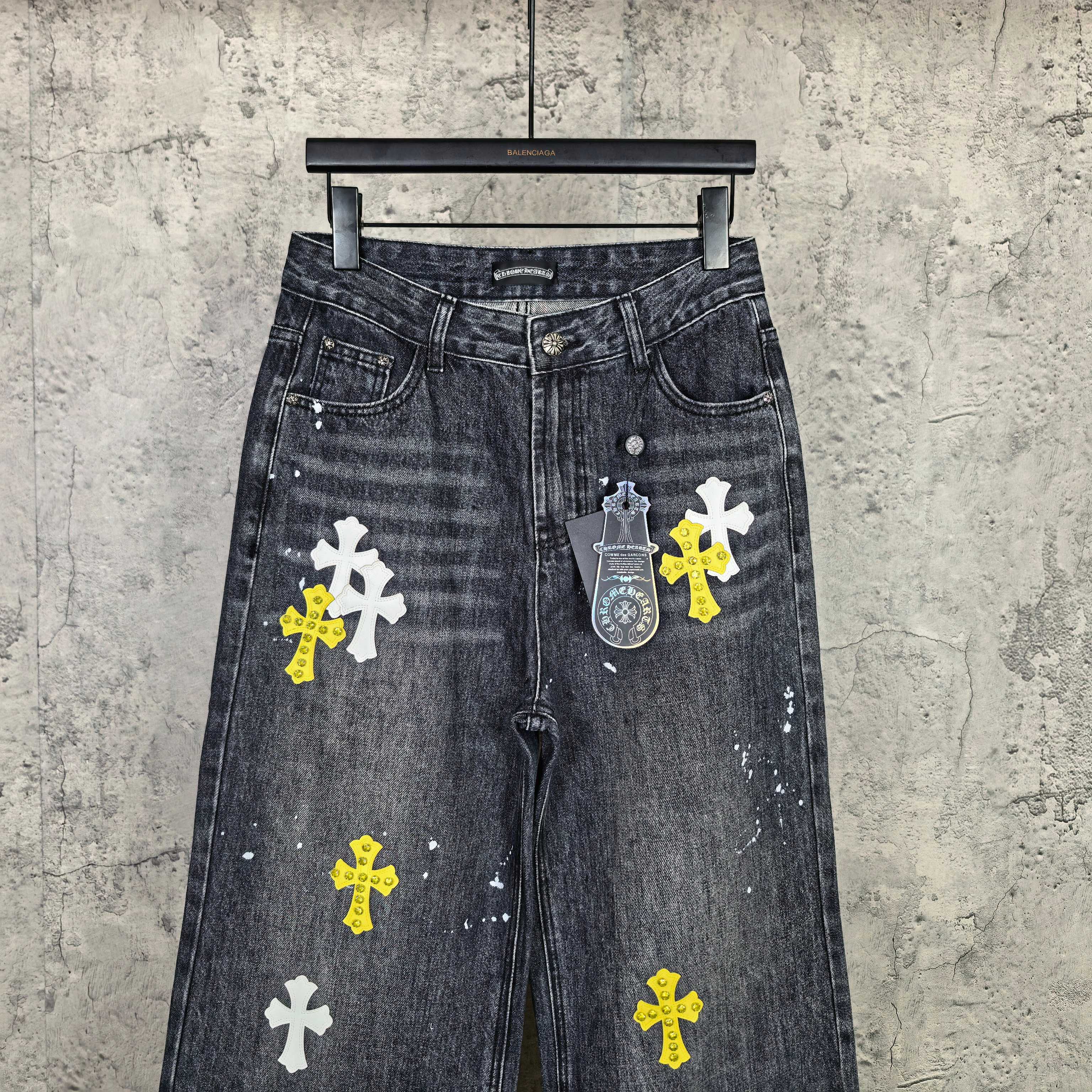 Dark denim pants with large cross prints, including yellow and white on legs