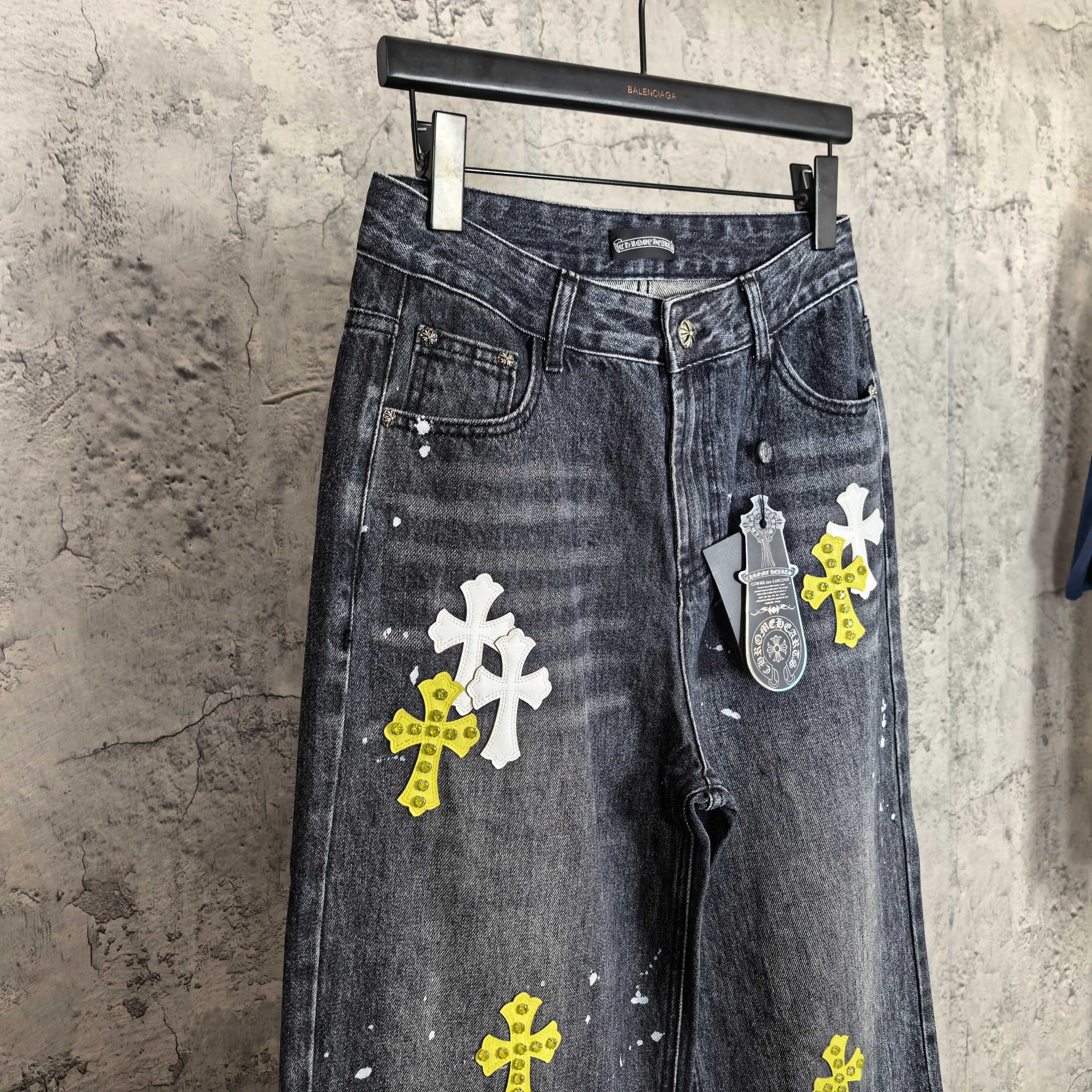 Dark denim pants with cross graphics and hanging tag print detail on right leg