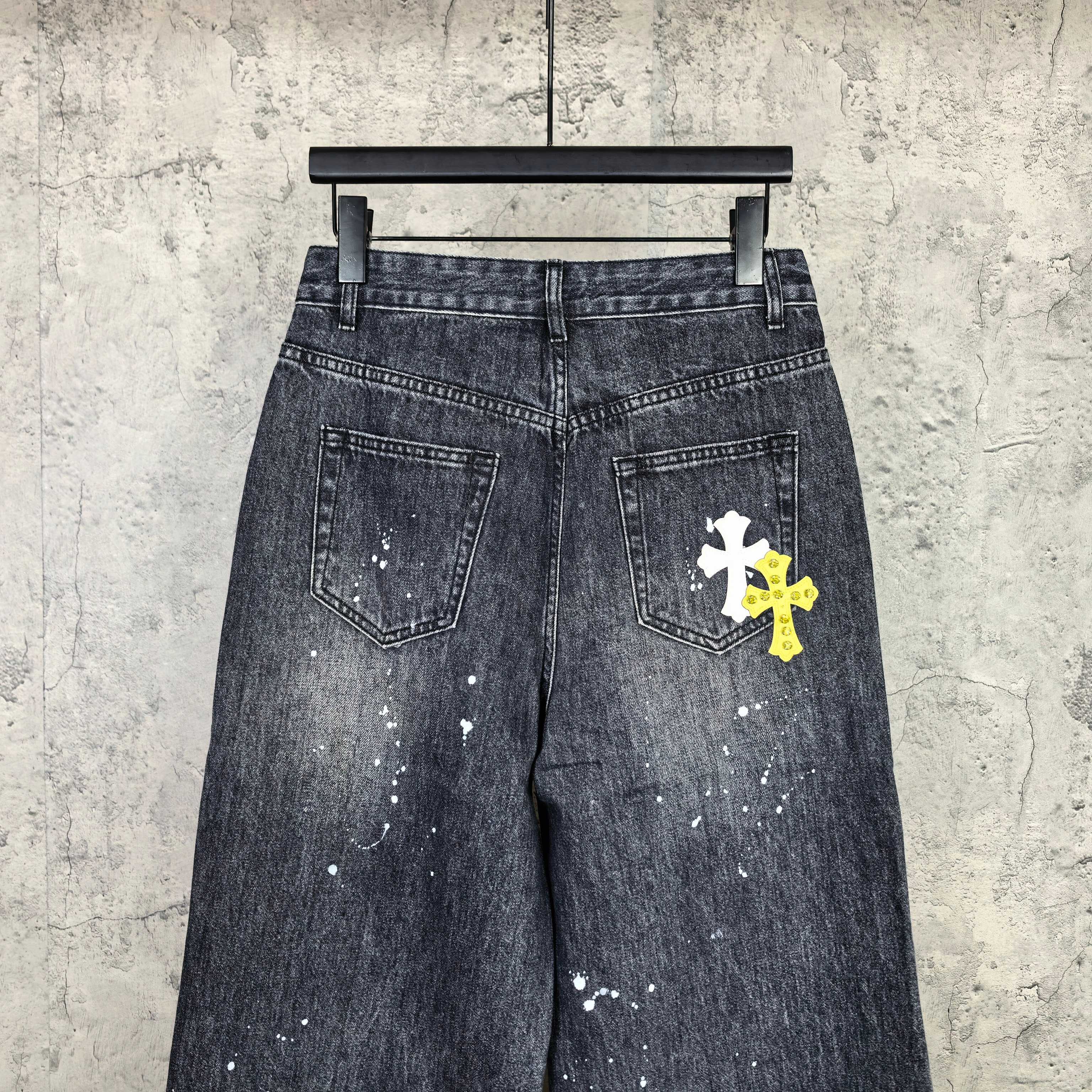 Dark denim pants with two front pockets and a white cross patch on right leg
