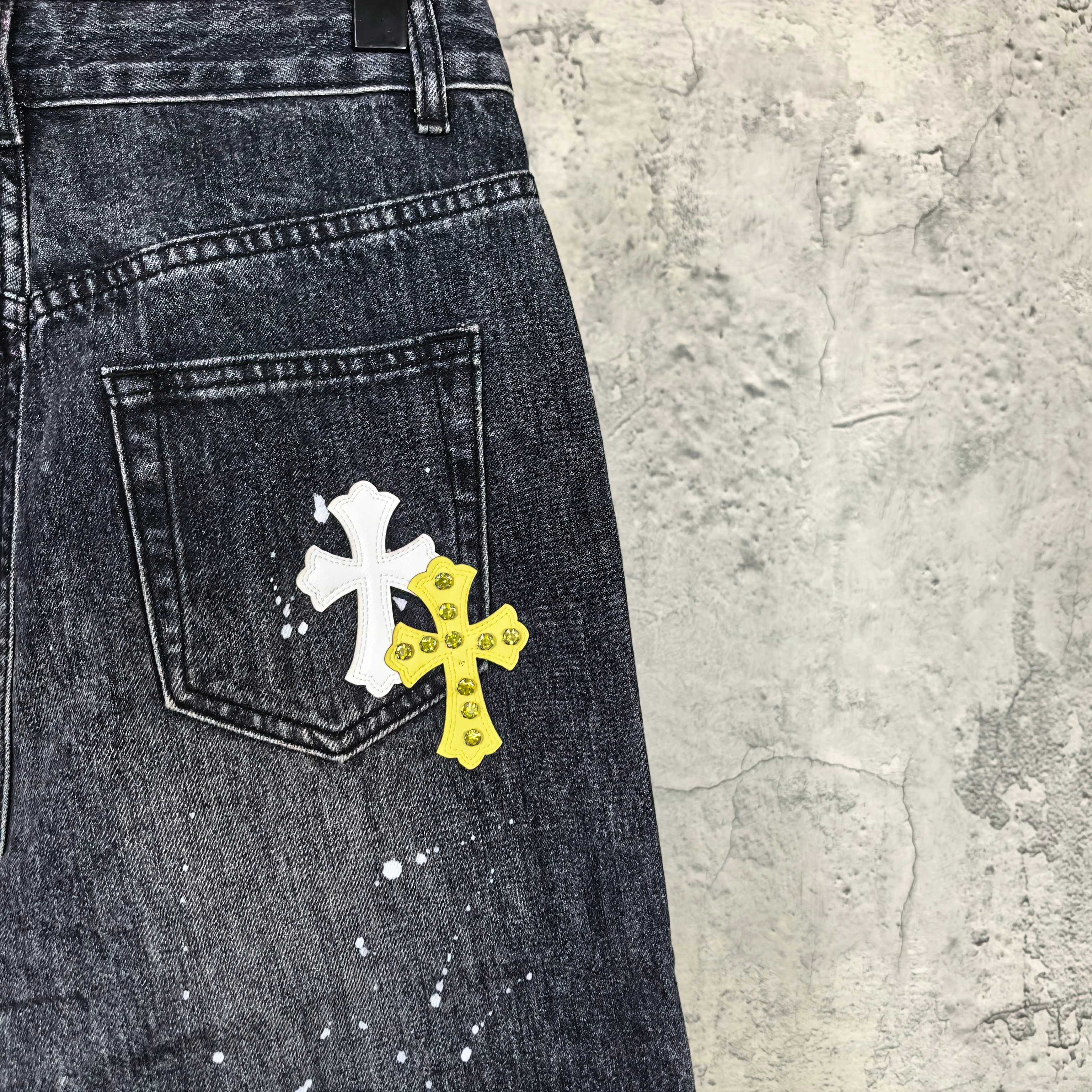 Dark denim pants with white and yellow cross patches on front pocket