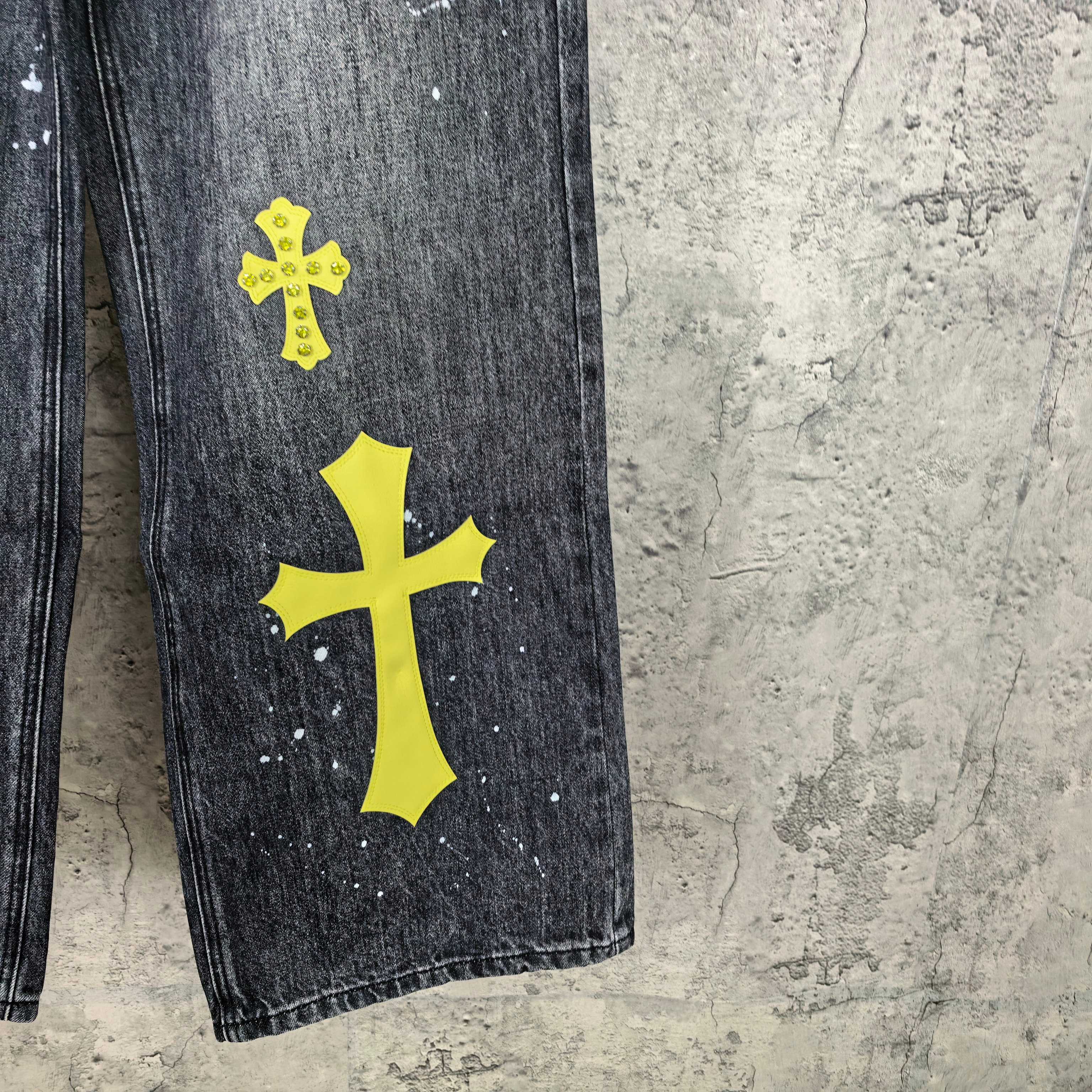 Dark denim pants with large yellow cross patch and white speckles