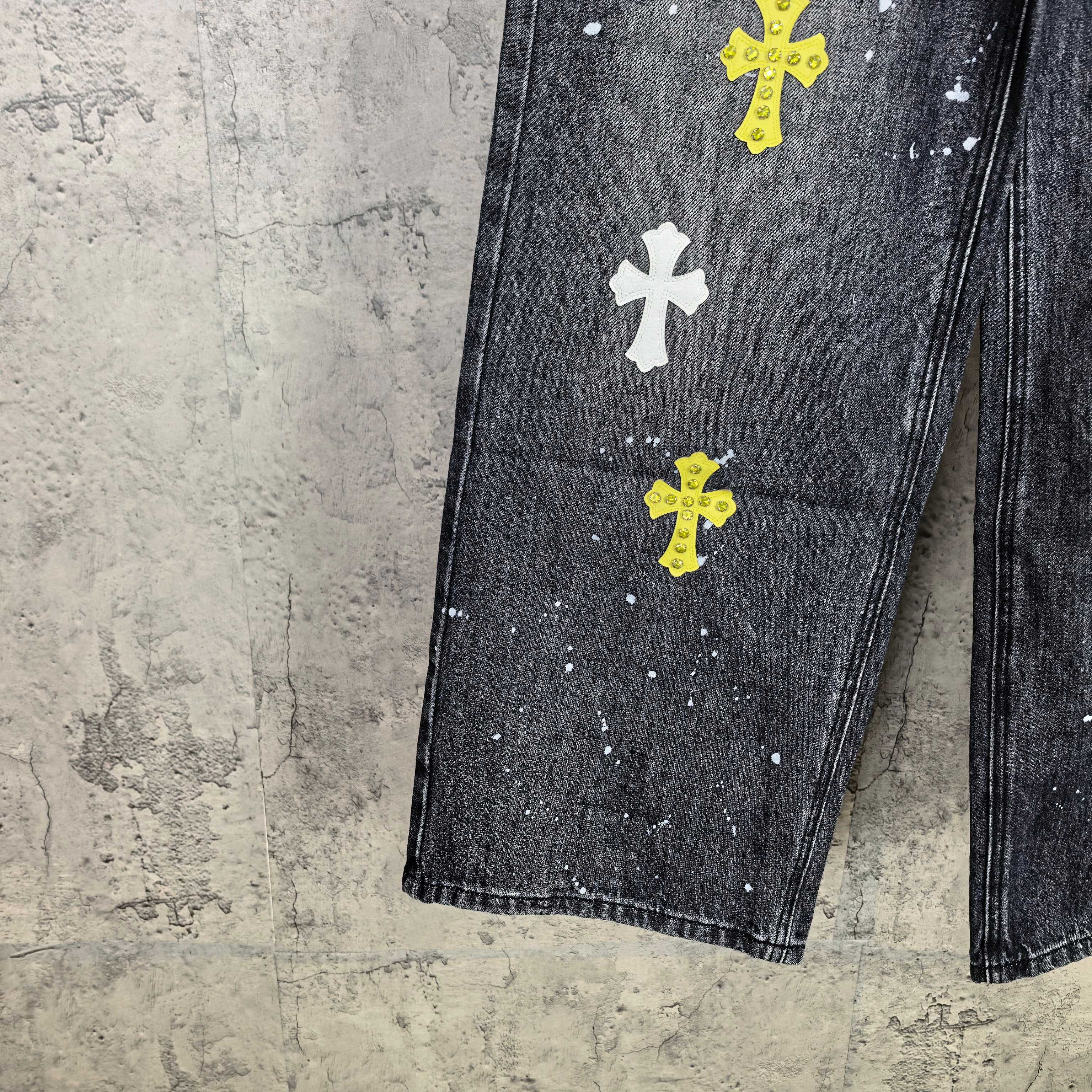 Dark denim pants with yellow and white cross graphics across leg