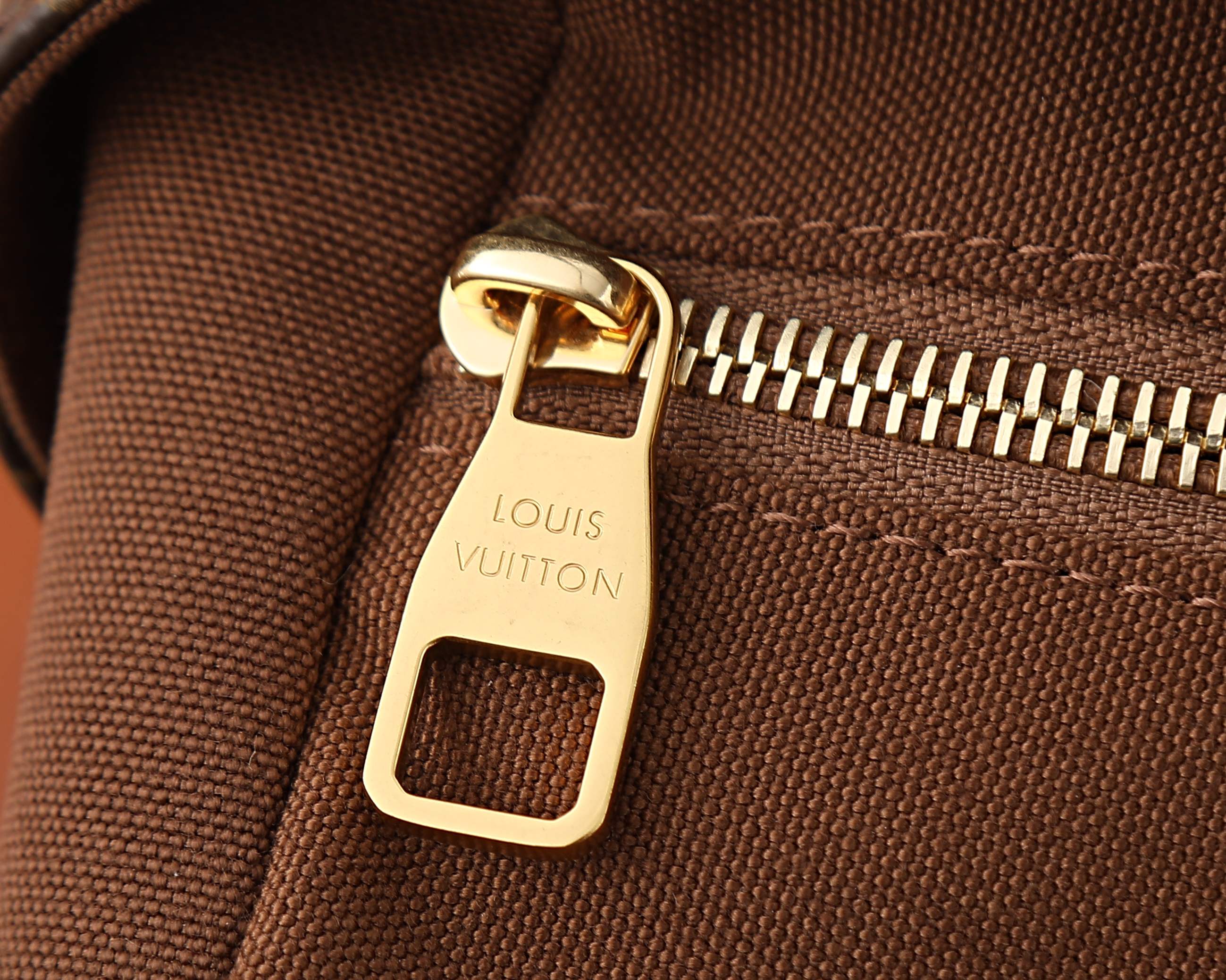 Gold-tone zipper pull on monogram crossbody bag with fabric texture