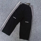 Black track pants with white side stripes and small logo text on leg