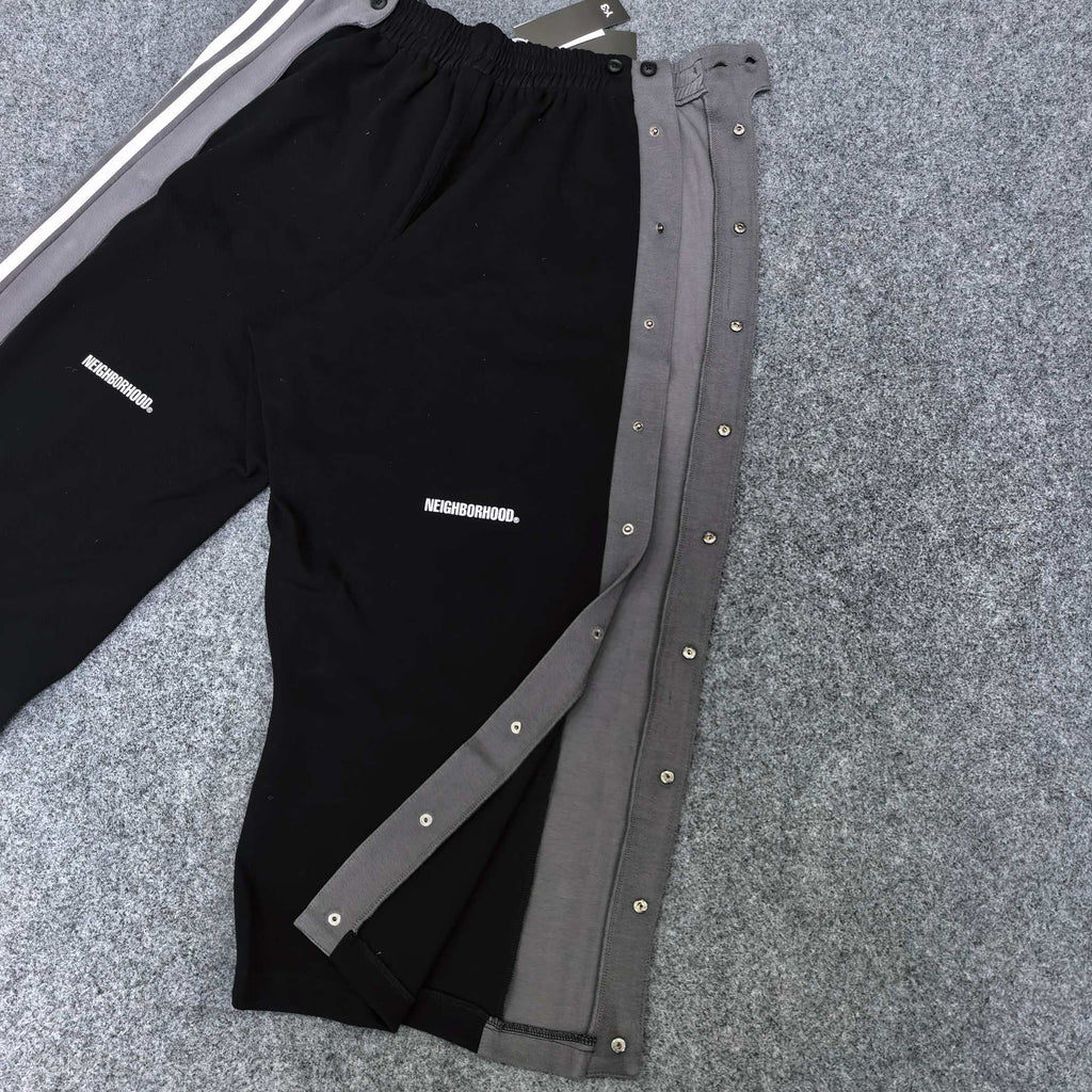 Black track pants with gray snap-button side panels and white stripe detail