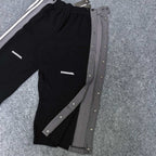 Black track pants with gray snap-button side panels and white stripe detail