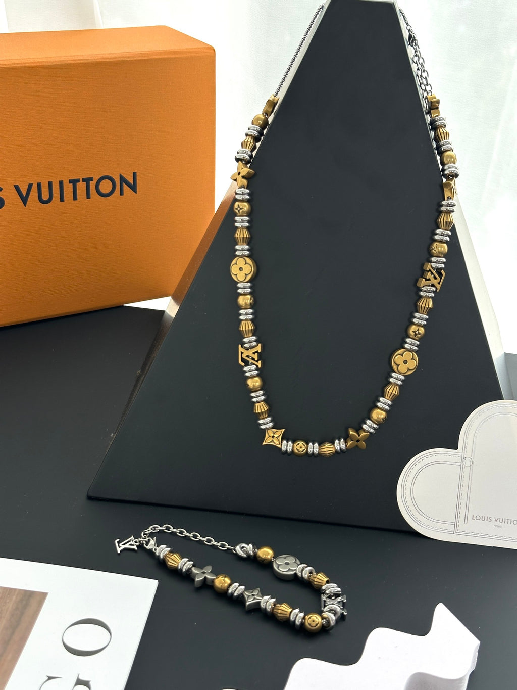 Gold and silver beaded charm necklace with matching bracelet on black display
