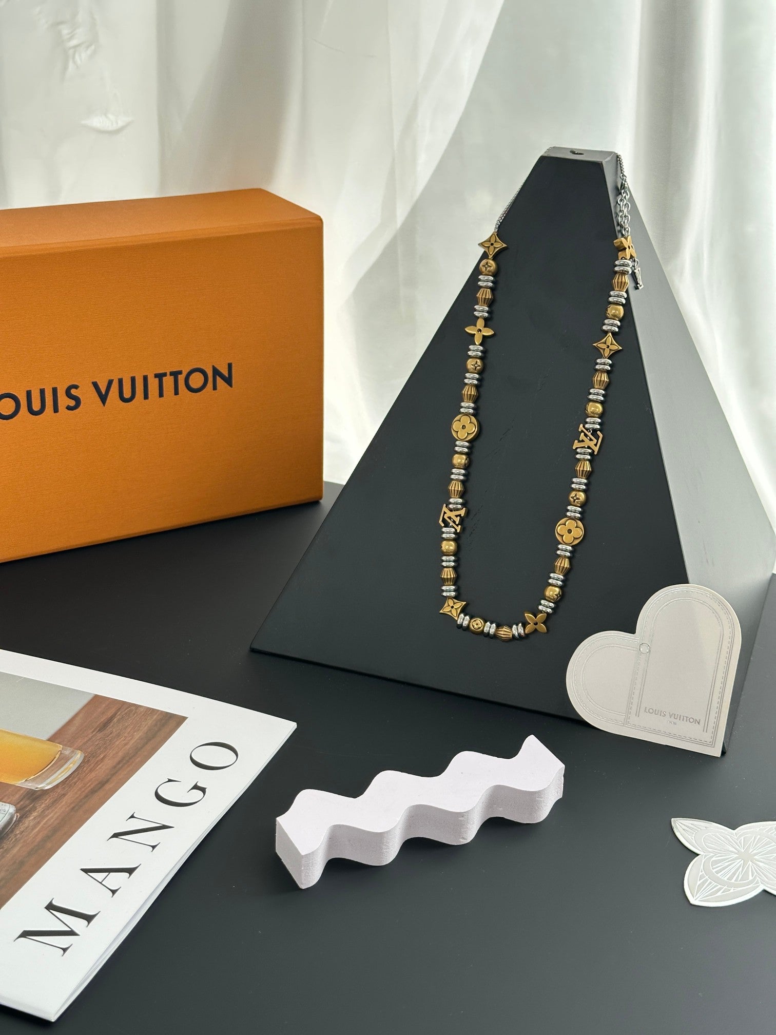 Louis Vuitton beaded necklace on a dark display stand with heart accessory