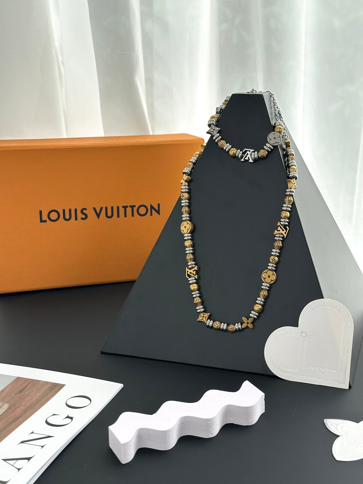 Louis Vuitton beaded necklace with gold and silver charms on a display stand