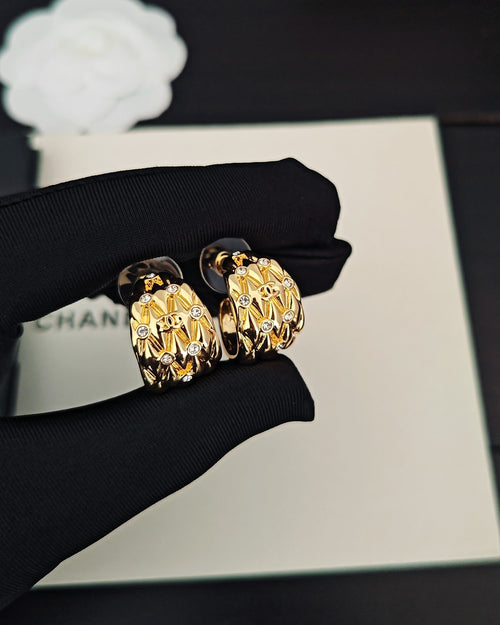 Gold-tone hoop earrings with crystal-like details, paired on dark pouch