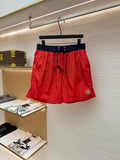 Red swim shorts with navy waistband and blue drawstring, front view on hanger