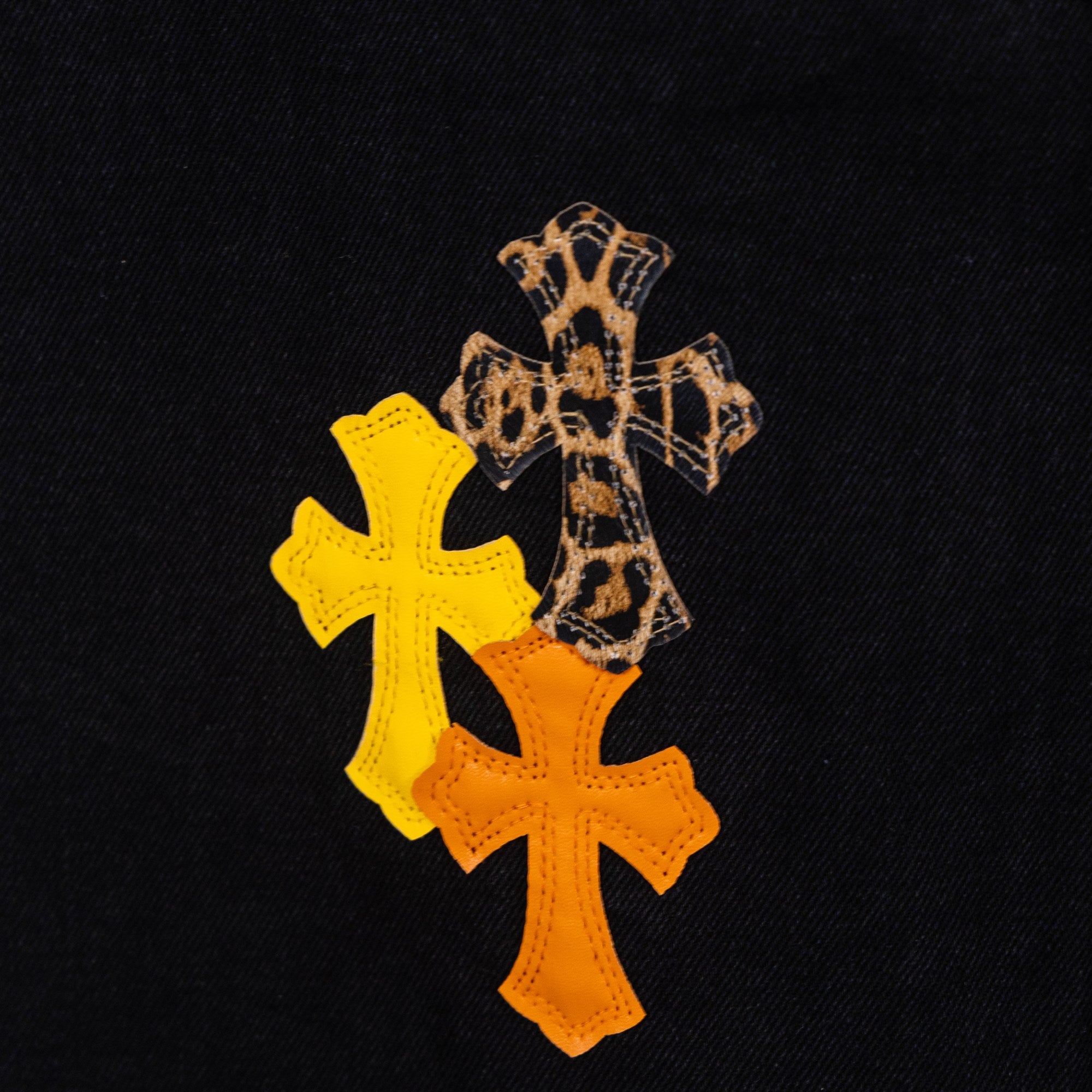 Close-up of orange and yellow cross embroidery on black denim fabric
