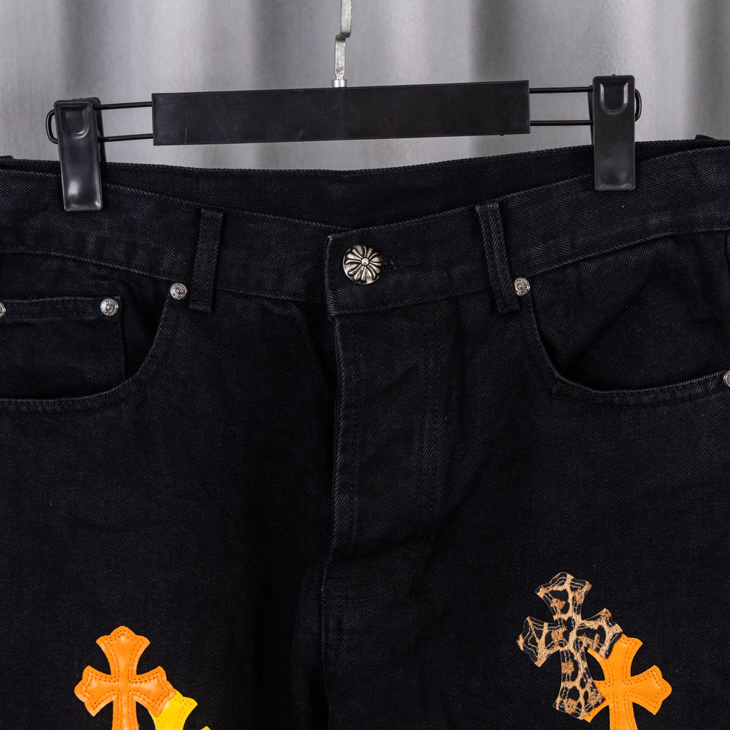 Front view of black denim pants with metal button closure and cross embroidery