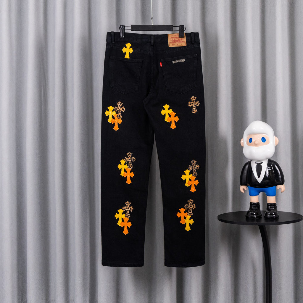 Black denim pants with scattered orange and yellow cross embroidery and logo patch