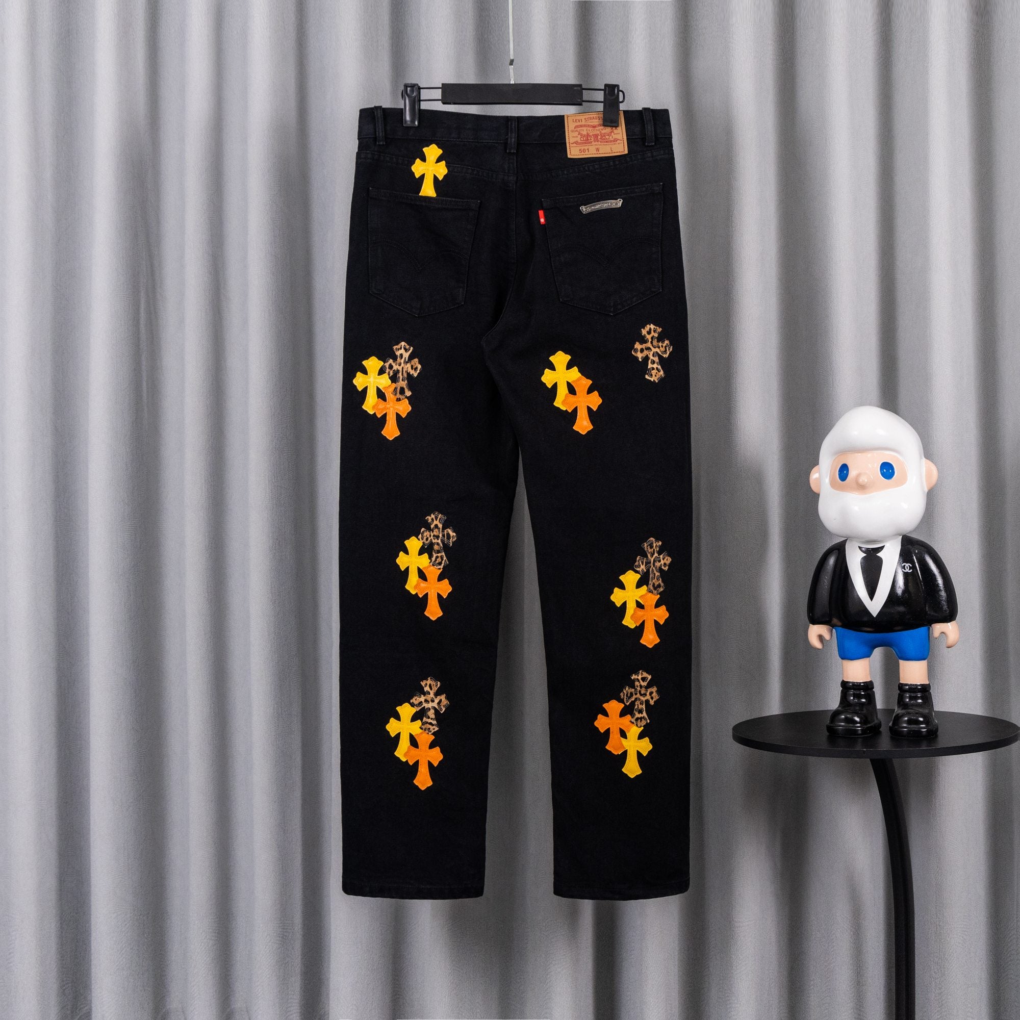 Black denim pants with scattered orange and yellow cross embroidery and logo patch
