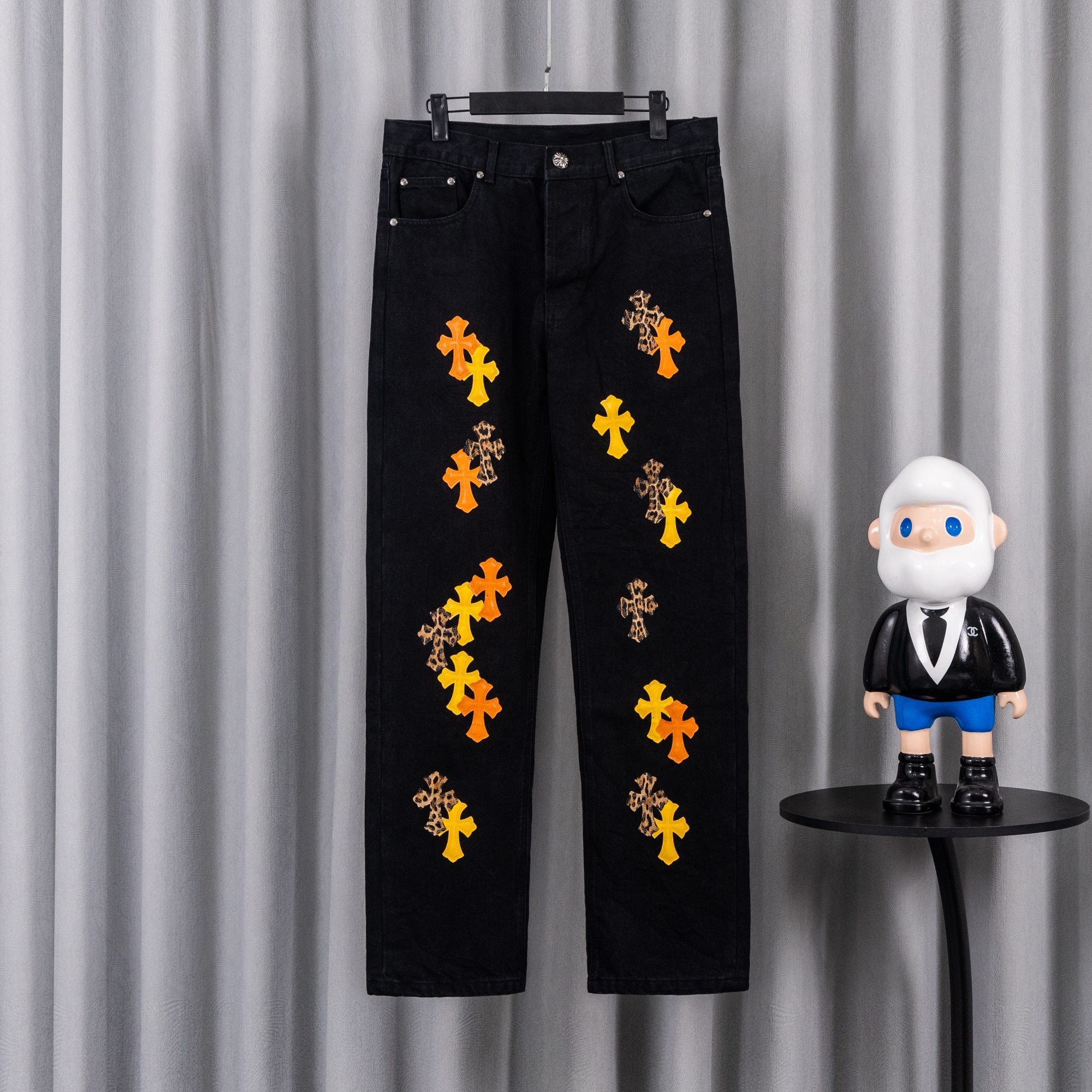 Black denim pants with orange and yellow cross embroidery on the legs