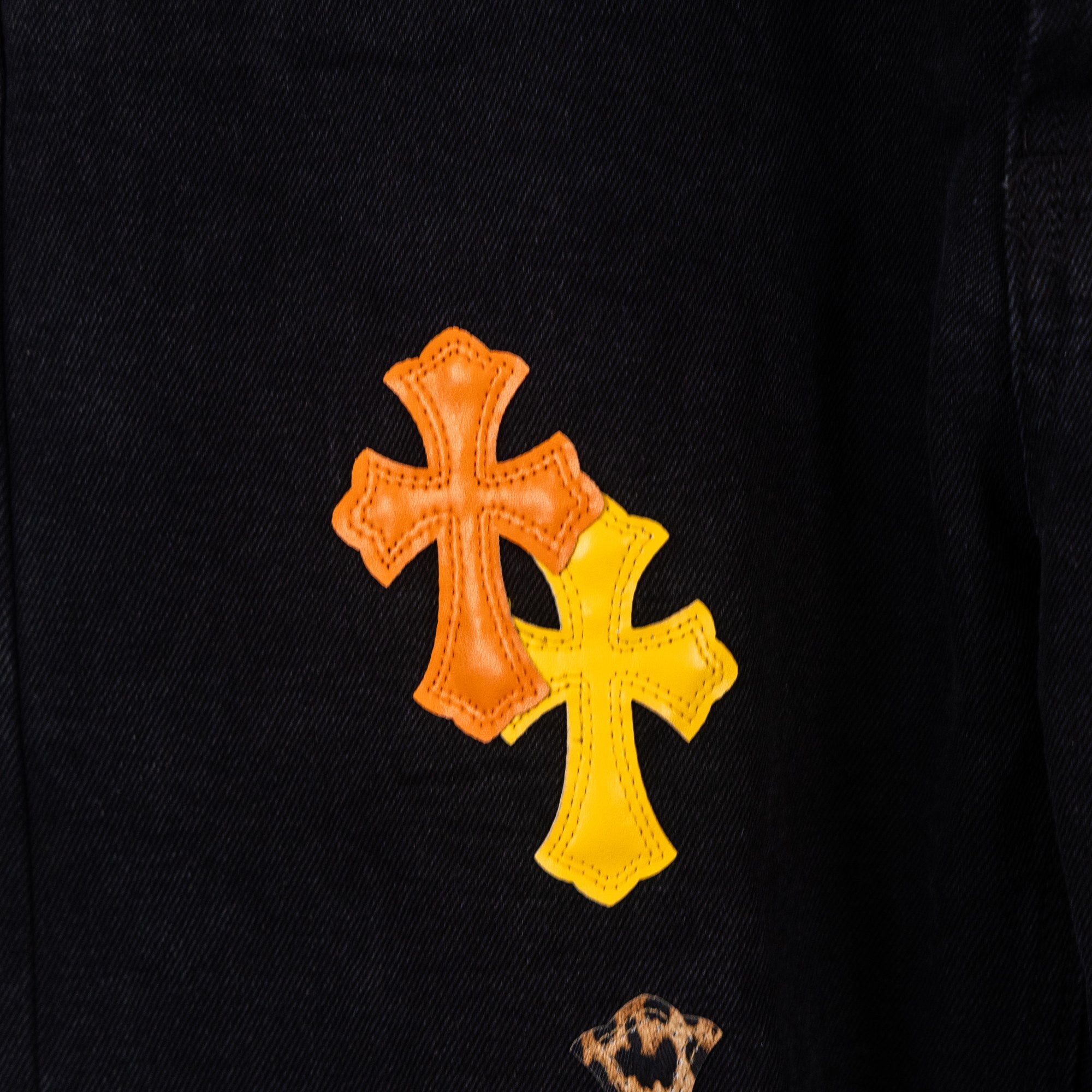 Close-up of orange cross patch detail on black denim pants