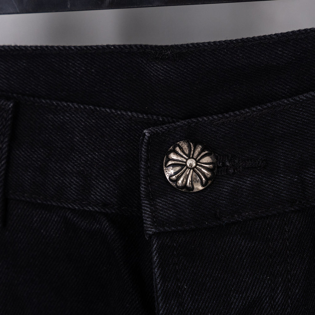 Close-up of black denim pants button with round metal decorative emblem