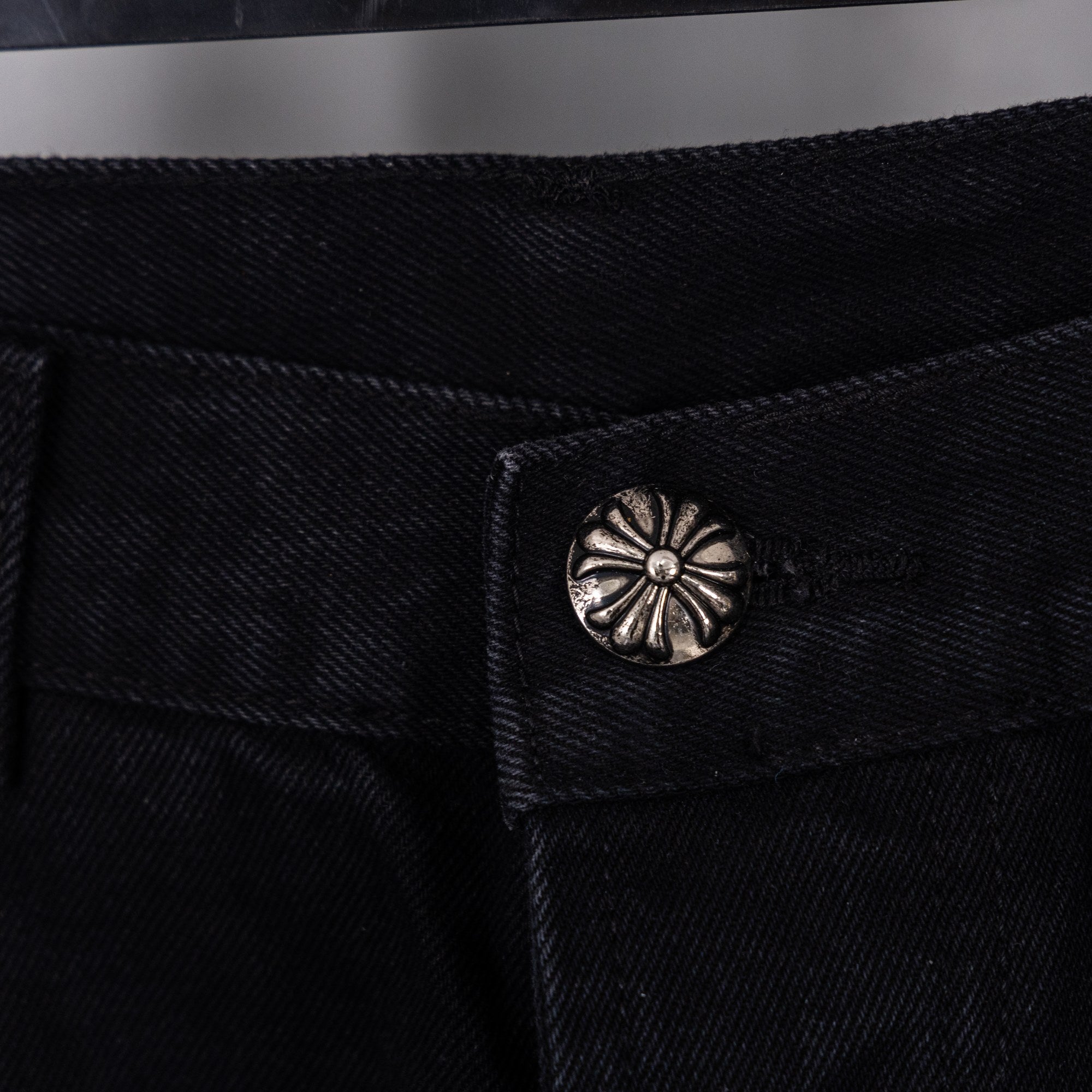 Close-up of black denim pants button with round metal decorative emblem