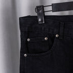Black denim pants front with button fly, pockets, and metal rivets
