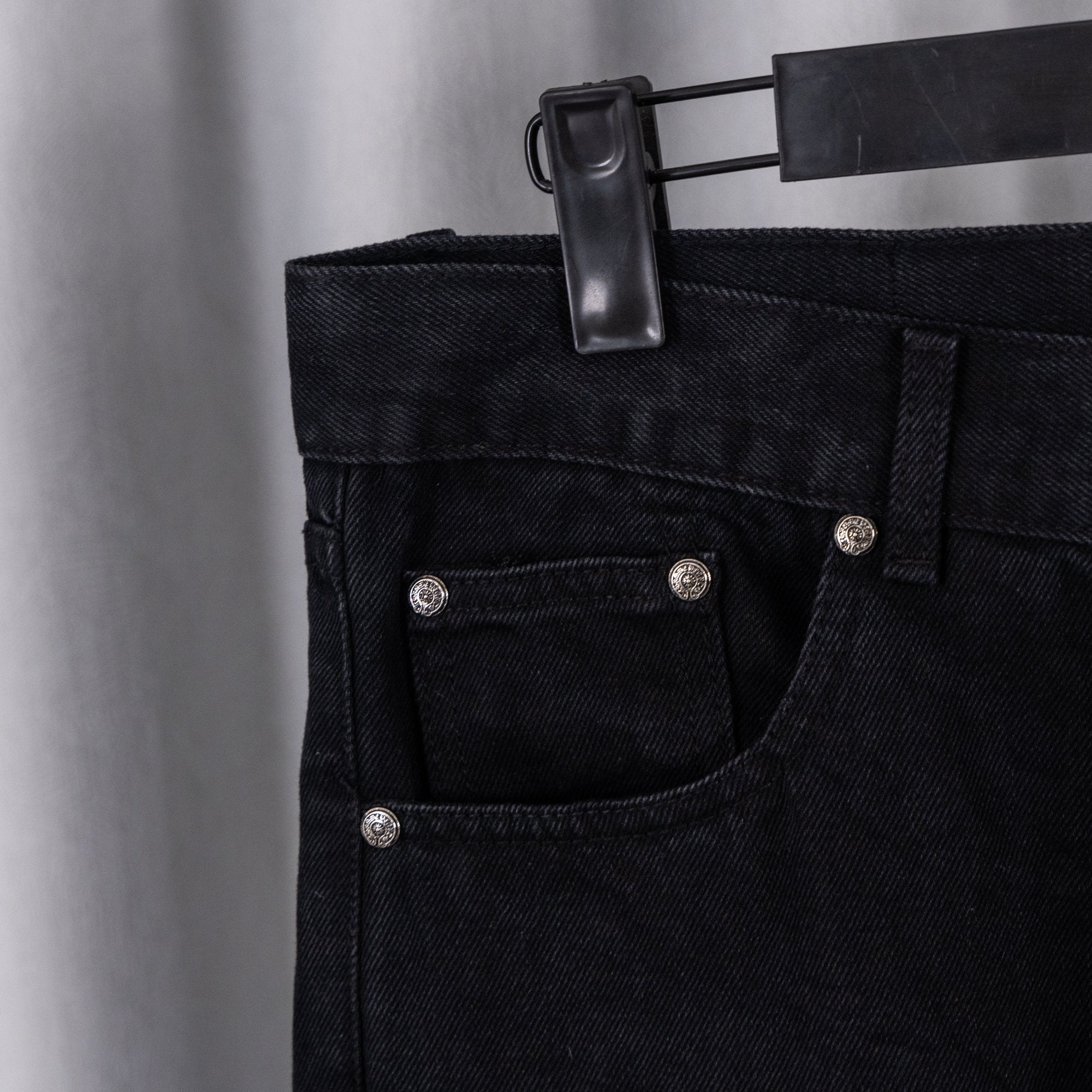 Black denim pants front with button fly, pockets, and metal rivets