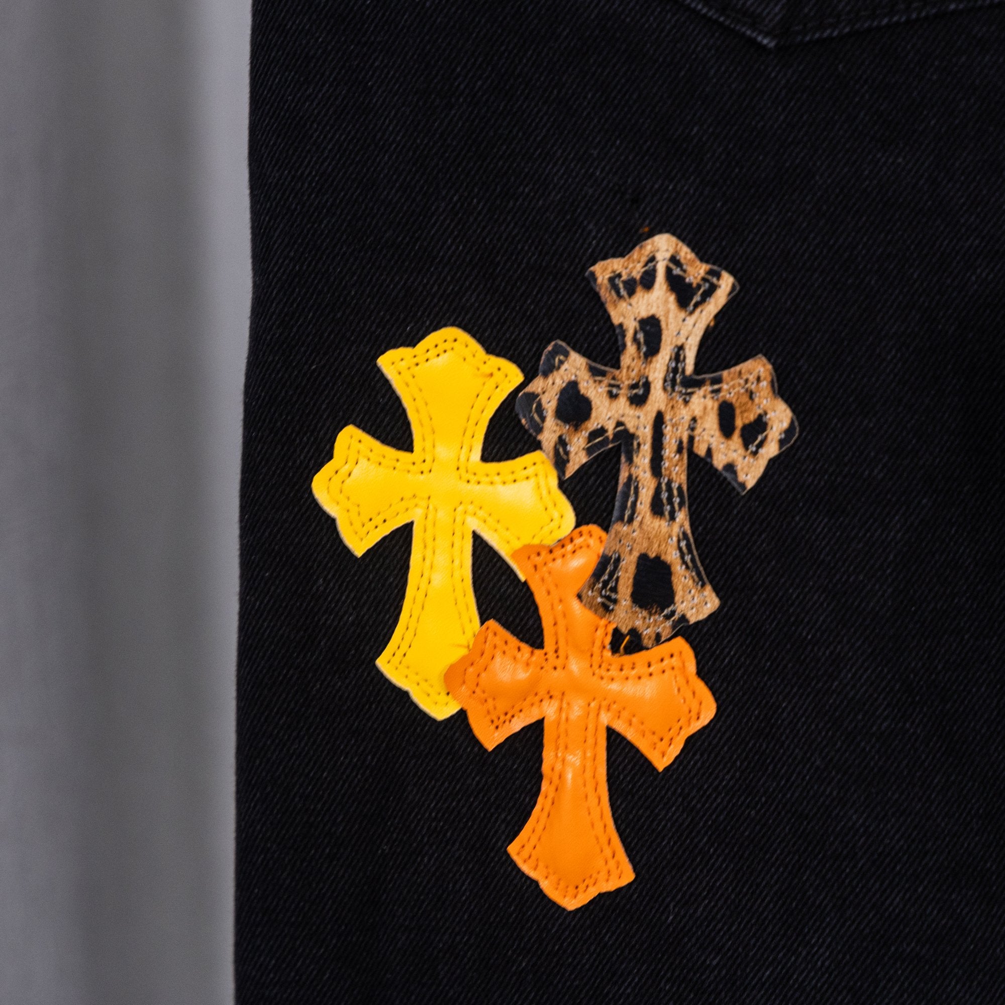Black denim pants with yellow and orange cross patches on the front