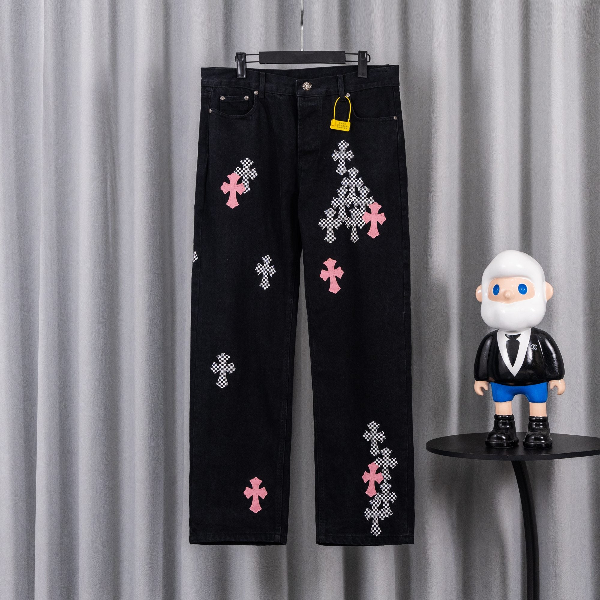 Black denim pants with pink and checkered cross patches, front view.