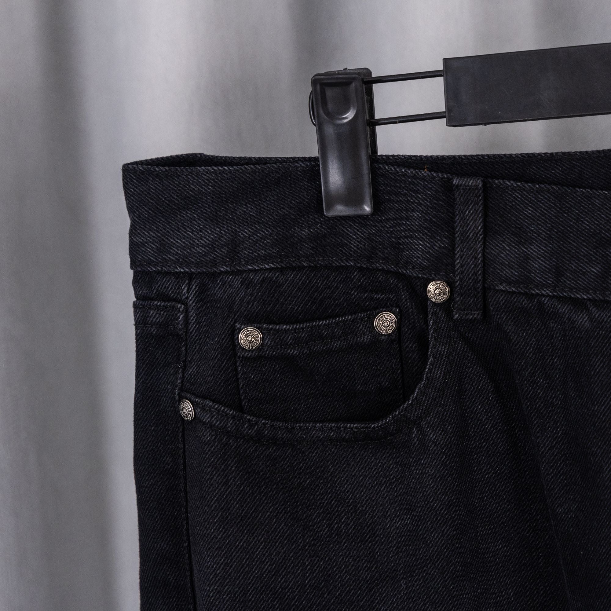 Black denim pants with buttoned front and pocket detailing.