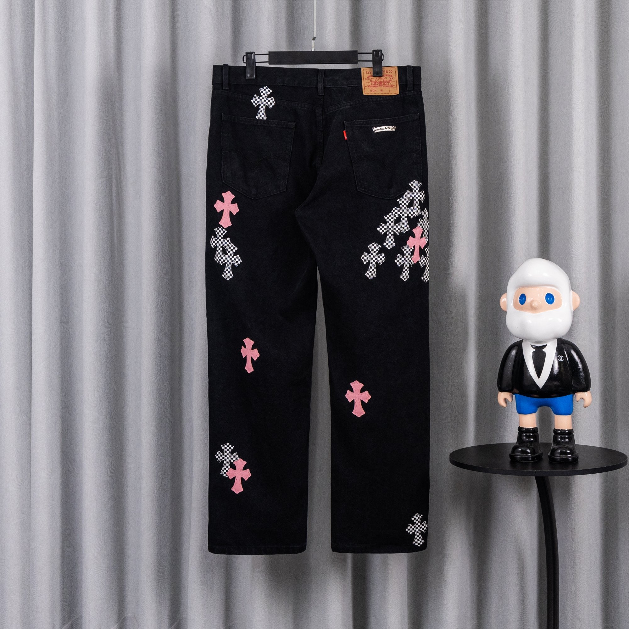 Black denim pants with pink and checkered cross patches, back view.
