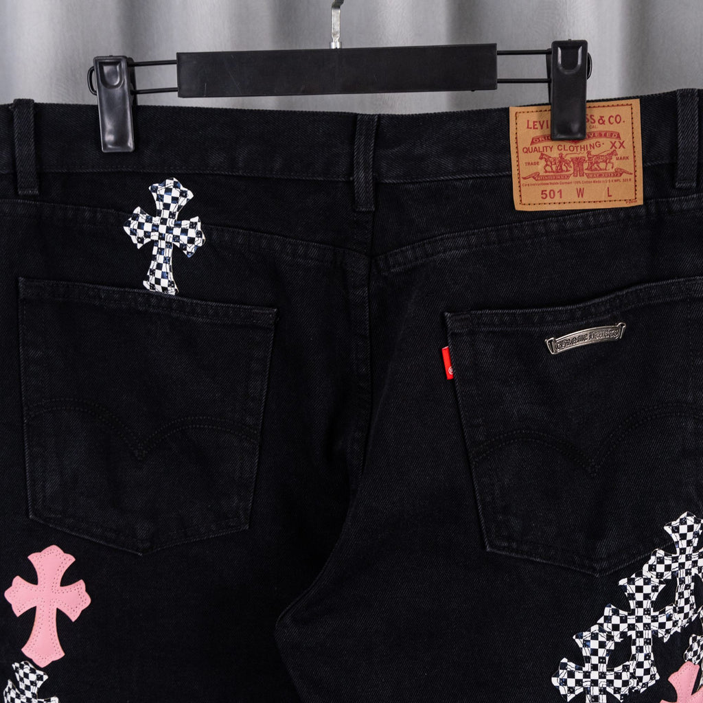 Black denim pants with side pockets, branded patch, and cross embroidery.