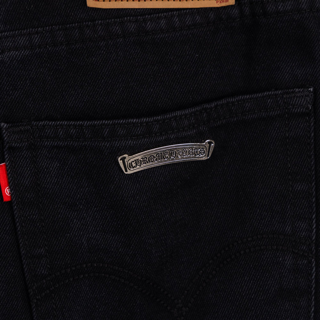 Black denim pants with small metal logo patch on front pocket area.