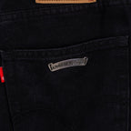 Black denim pants with small metal logo patch on front pocket area.