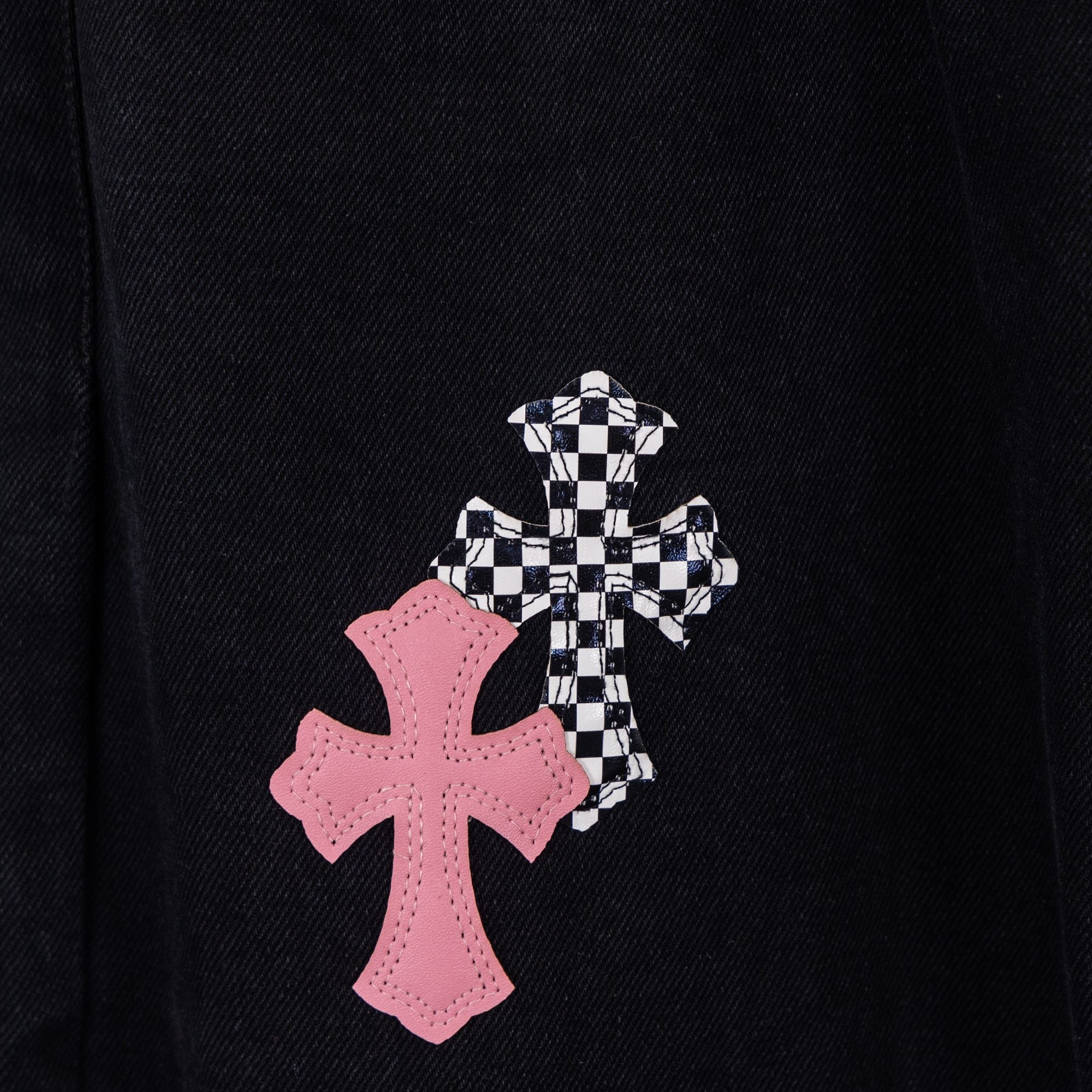 Black denim pants with large pink cross and checkered cross patch on leg.