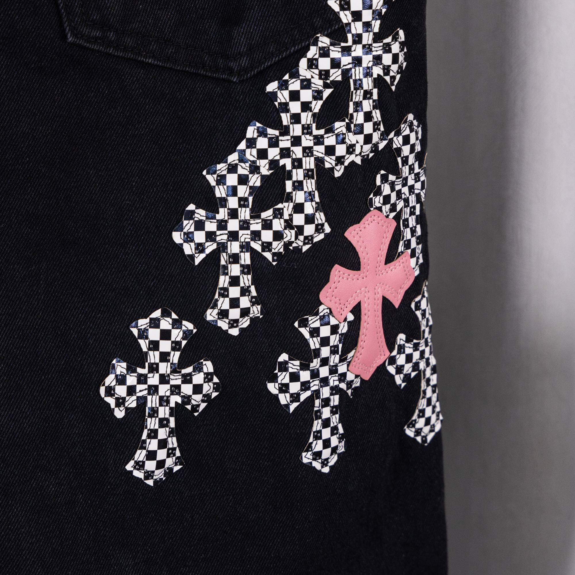 Black denim pants with multiple checkered cross patches and pink cross accents.