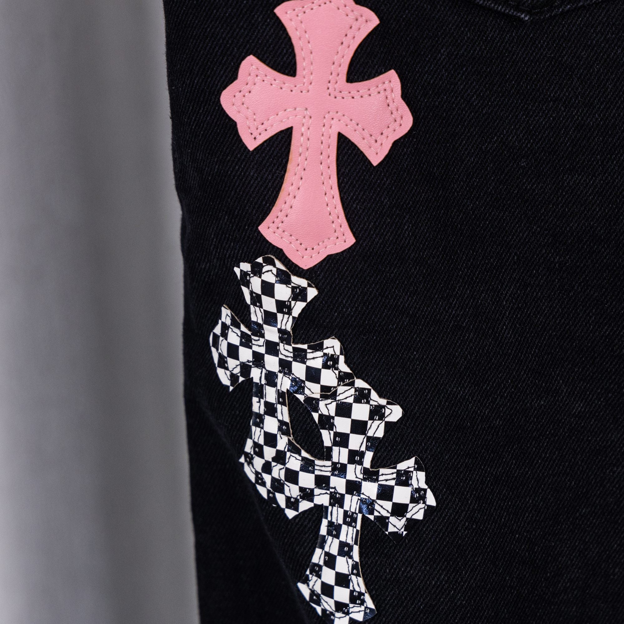 Black denim pants with pink cross patch above checkered cross patch.