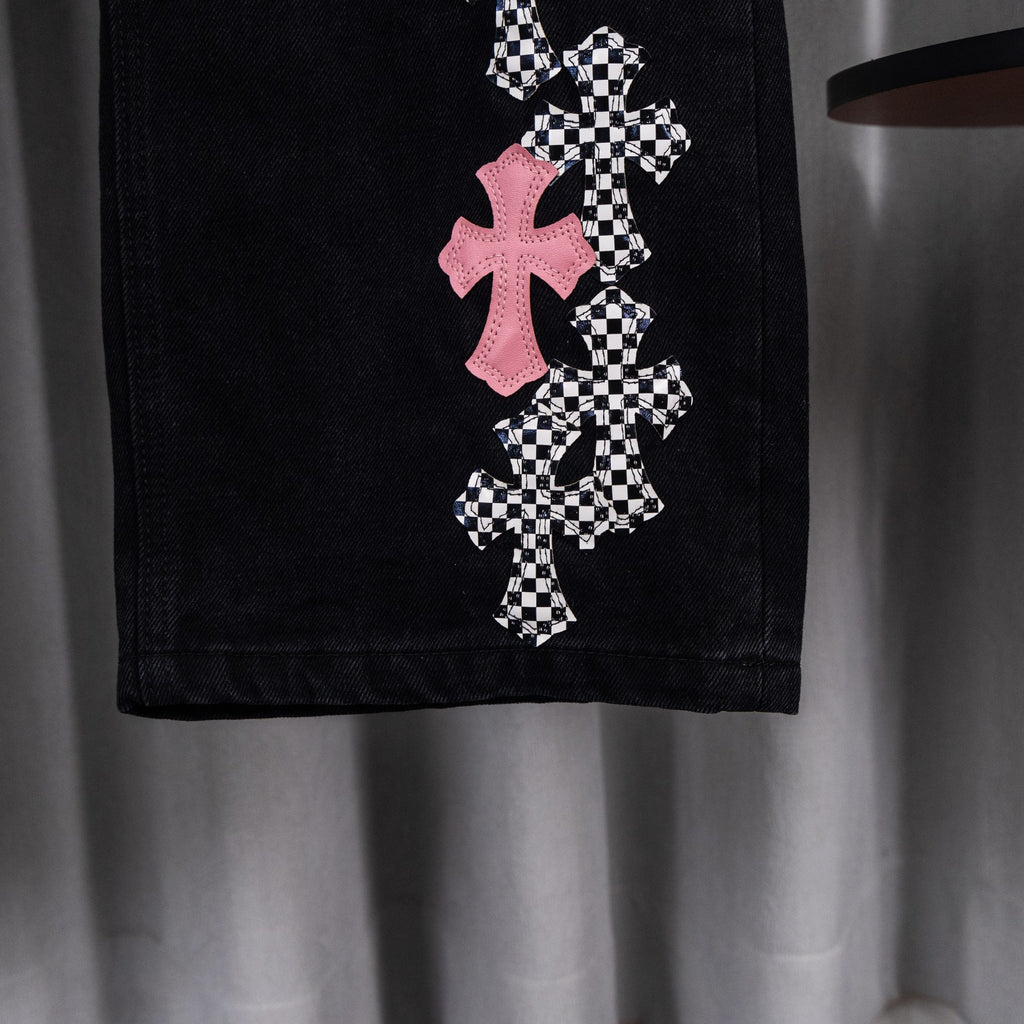 Black denim pants with pink and checkerboard cross appliques on one leg