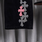 Black denim pants with pink and checkerboard cross appliques on one leg