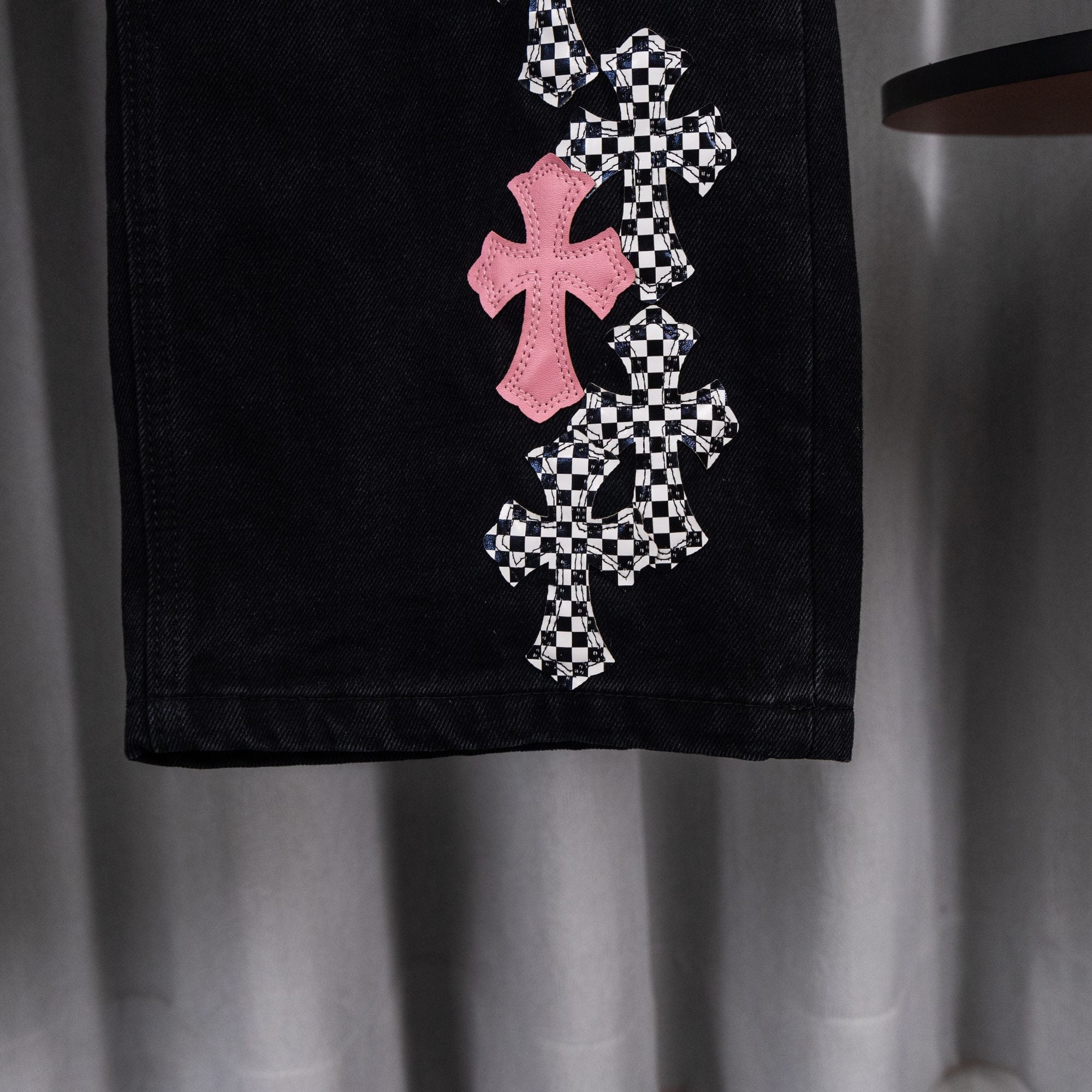 Black denim pants with pink and checkerboard cross appliques on one leg