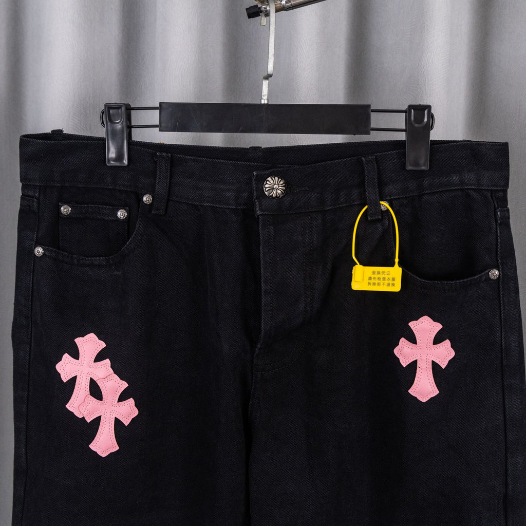 Dark denim pants with pink cross patch prints and a yellow hang tag at waist.