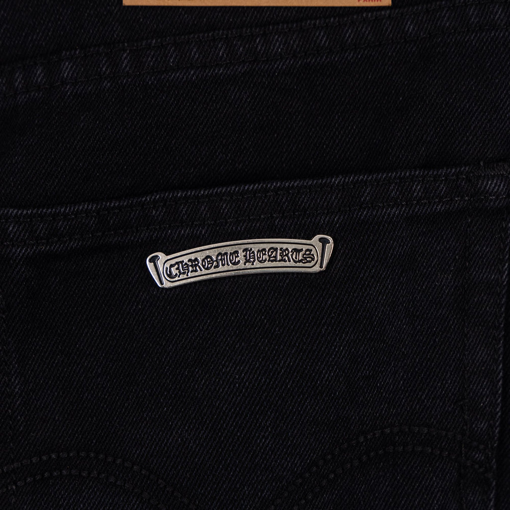 Metal logo patch on dark denim pocket seam, small rectangular tag.