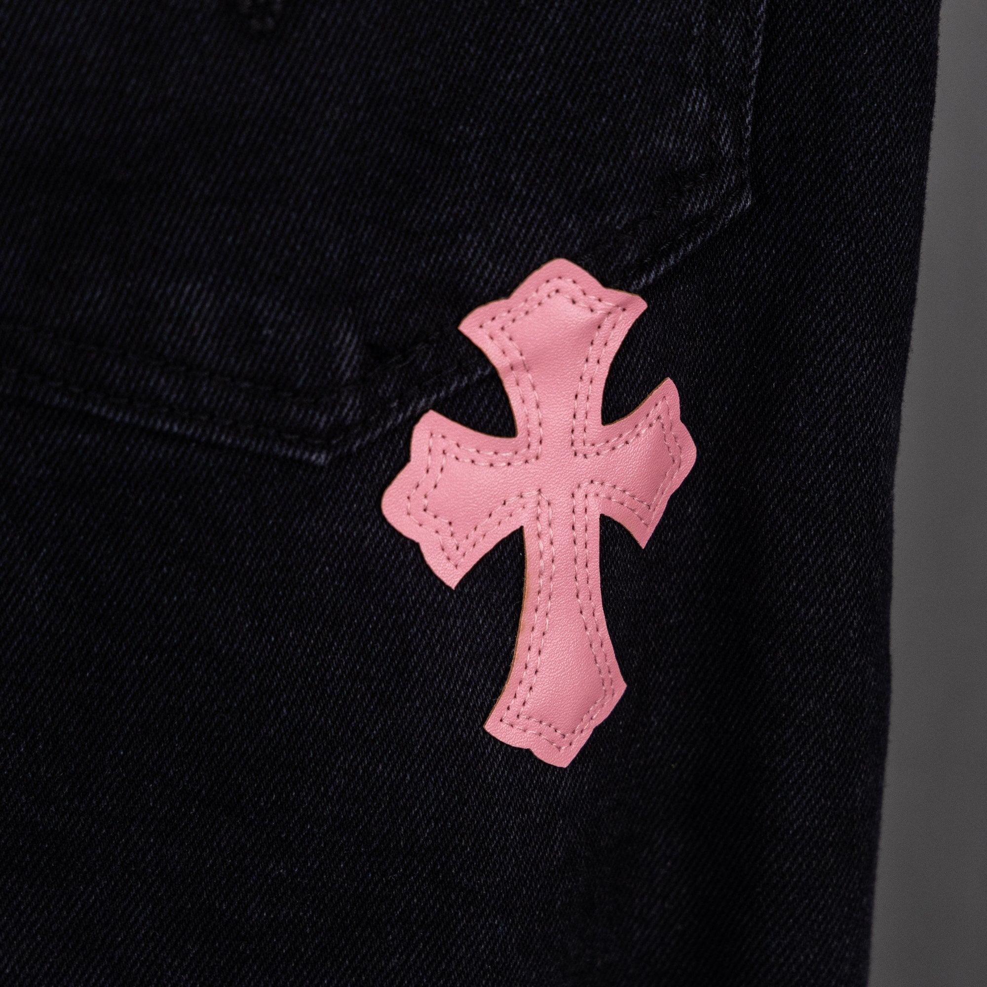 Pink cross applique on dark denim near pocket seam.