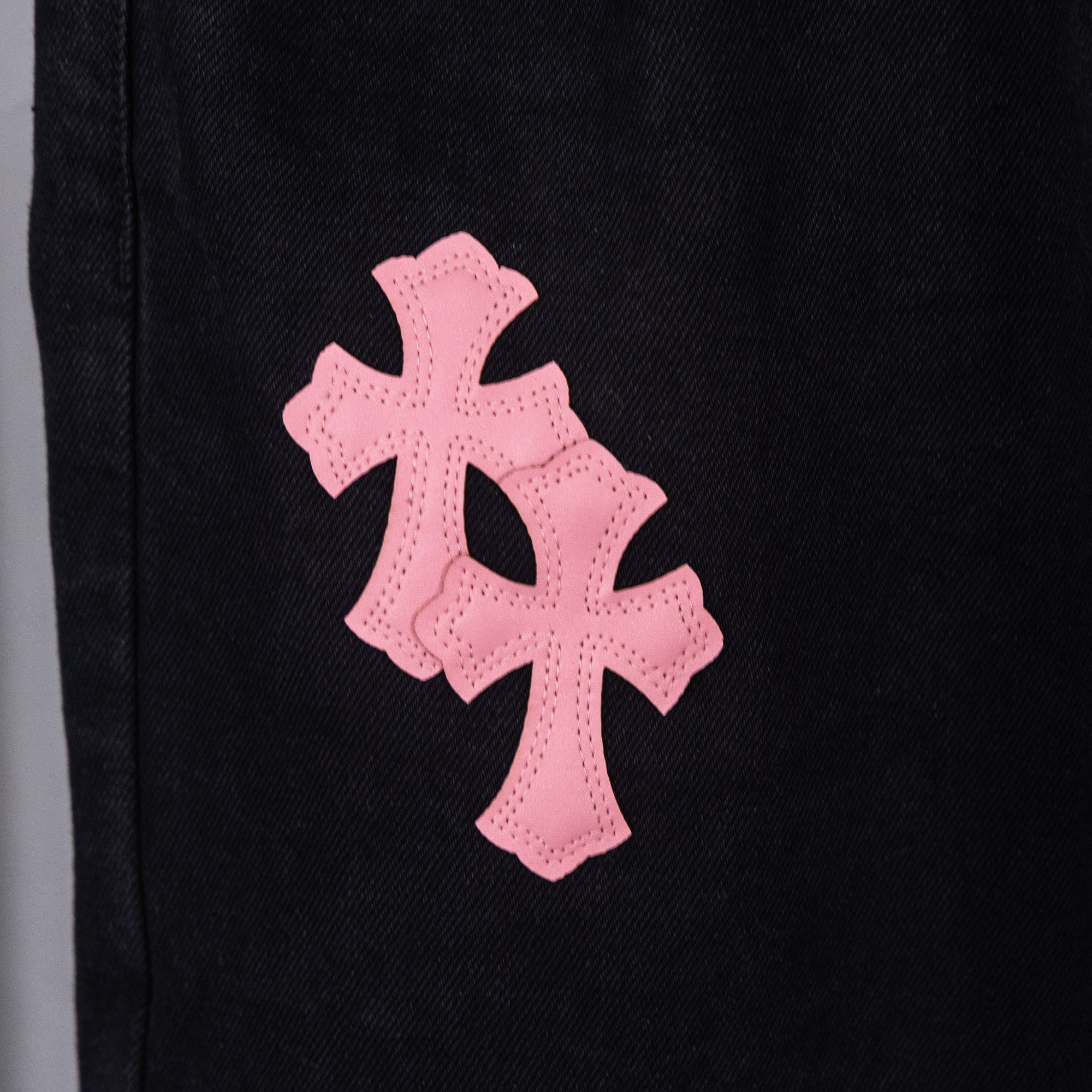 Pink cross applique on dark denim pant leg.
