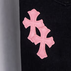 Large pink cross applique on dark denim pant leg.