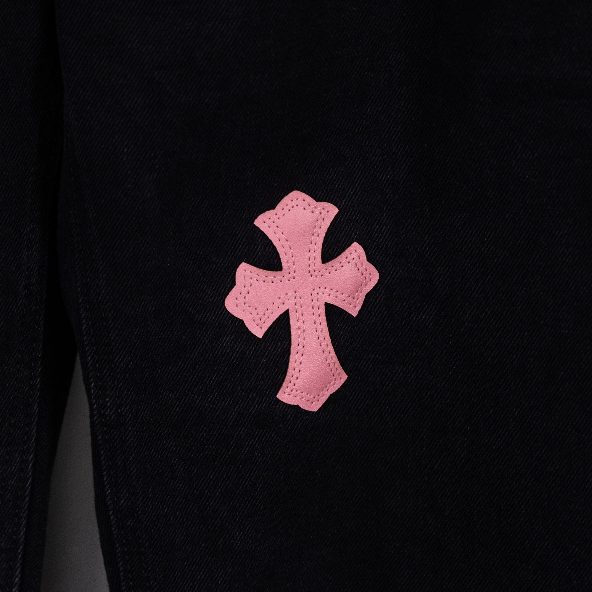 Black denim pants with large pink cross patch on leg