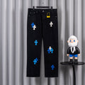 Black denim pants with blue and white cross appliques, five-pocket style.