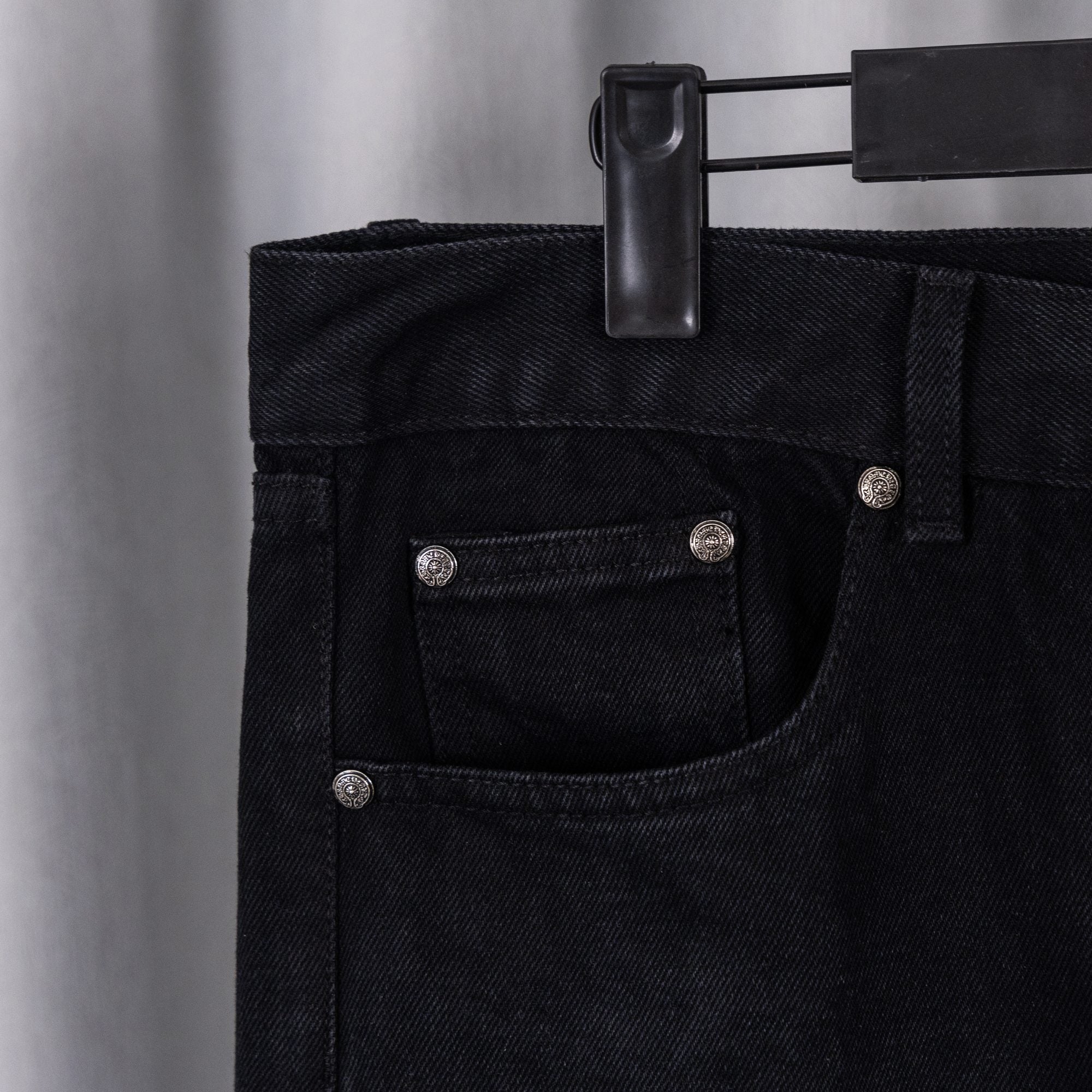Black denim pants waistband with belt loops and buttoned front pocket.