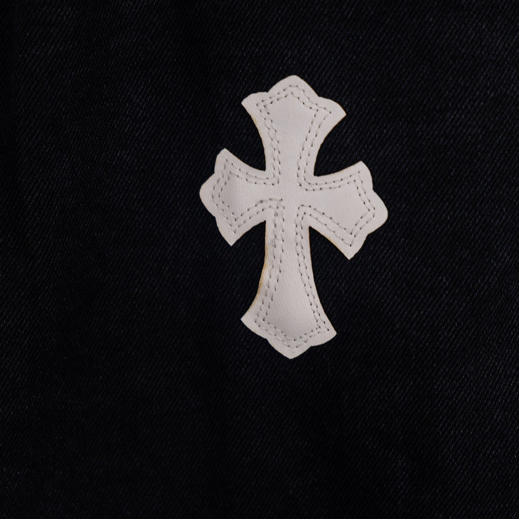 White cross applique on black denim pants fabric, close-up.