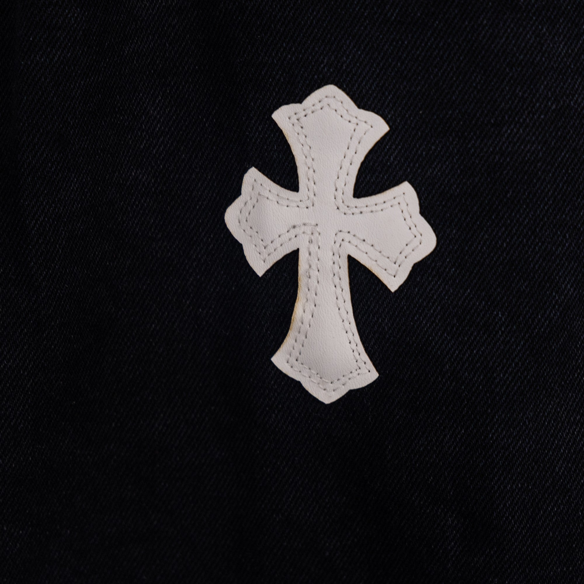 White cross applique on black denim pants fabric, close-up.
